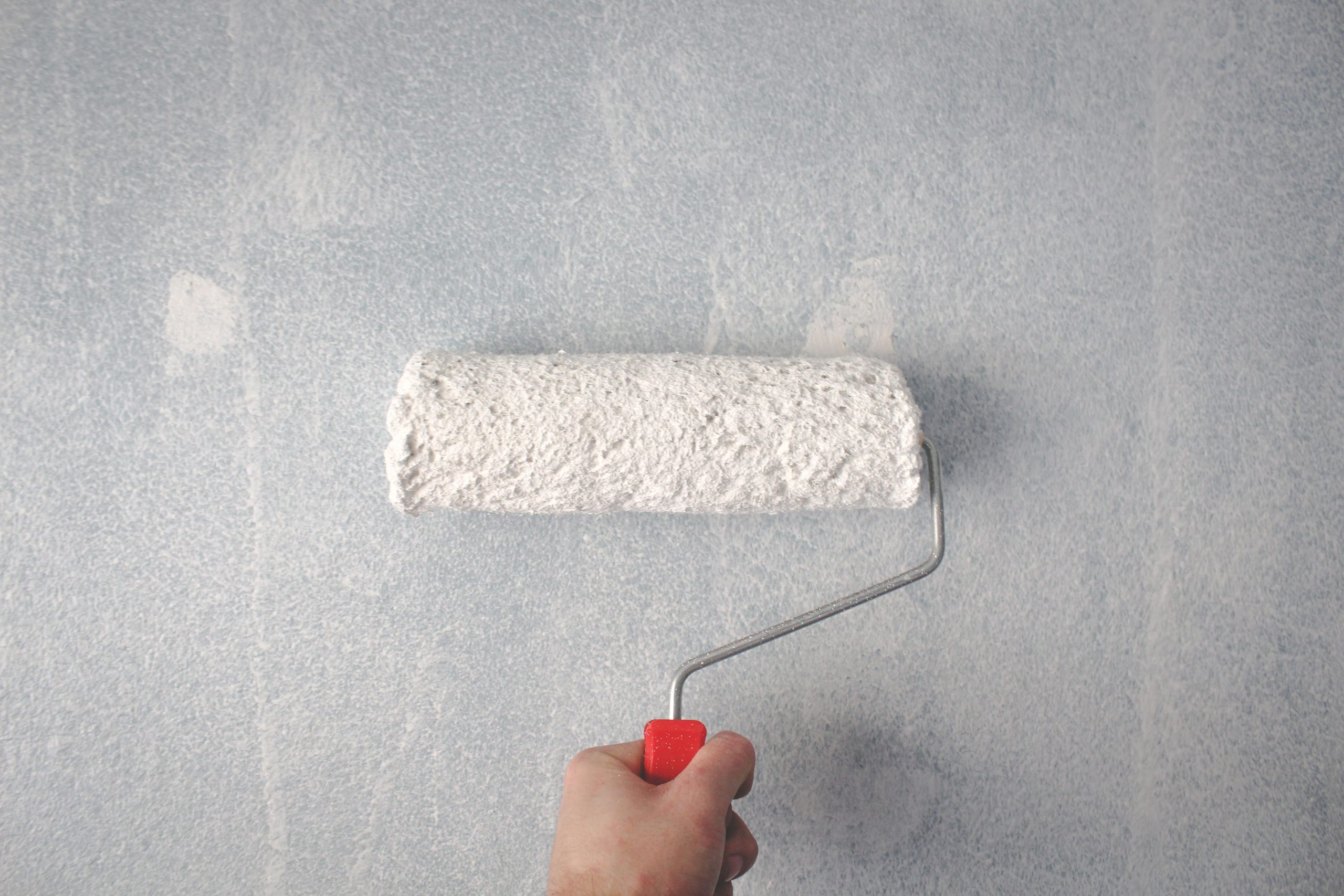 Main utilisant un rouleau pour peindre un mur blanc