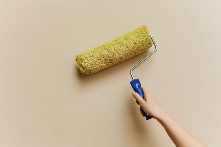 Main appliquant de la peinture beige au rouleau